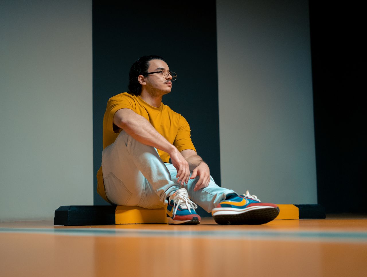 Services Young man in a yellow shirt sitting on a colorful gym floor, looking contemplative indoors.