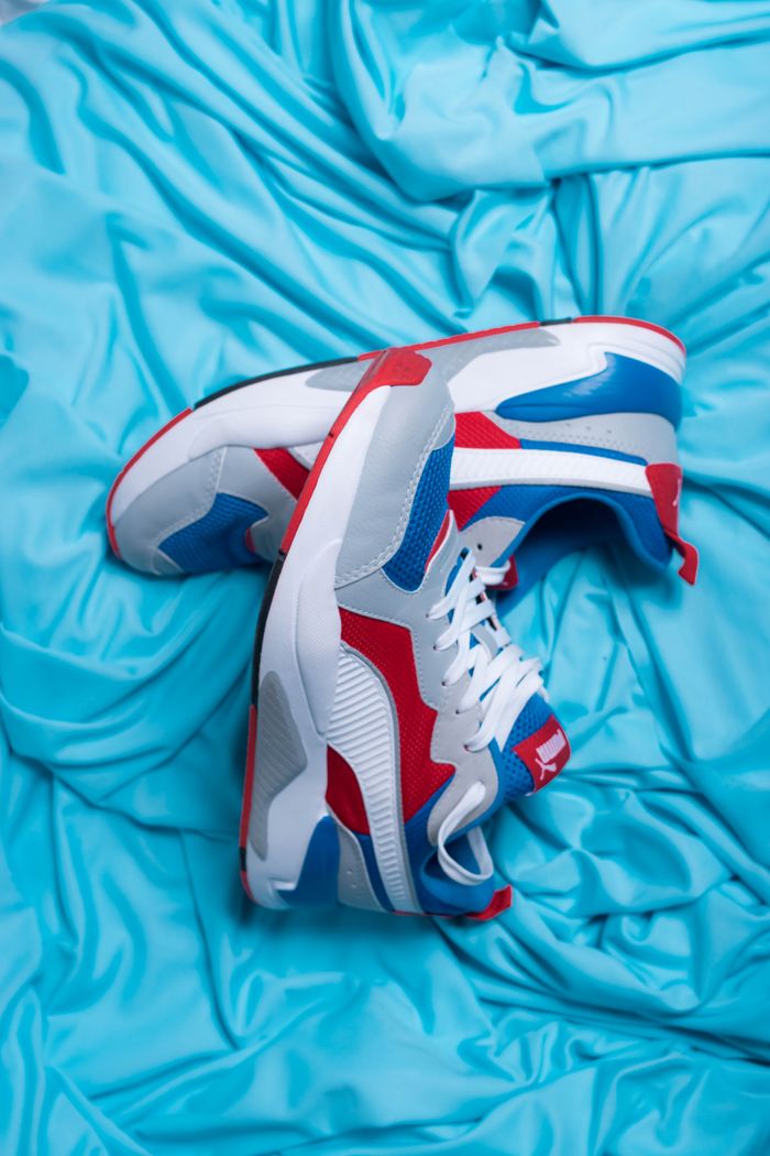 Home Top view of pair of modern sneakers with bright red and blue parts on creased cloth
